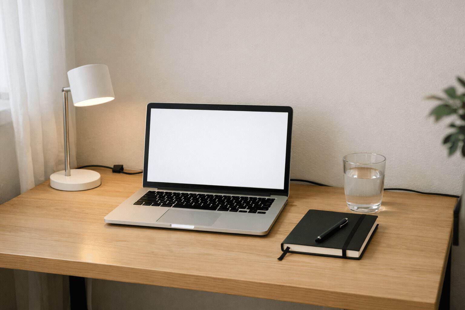 Minimal desk setup ideas for remote work in a small apartment with a laptop, lamp, notebook, water glass, and tidy cables.