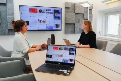 A woman uses a small wearable recorder in a meeting room, showing AI gadgets in 2026 at work.