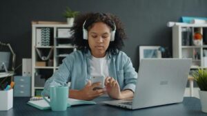 Person at a home office desk using earbuds and a voice assistant, showing AI wearables in daily life 2026.