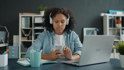 Person at a home office desk using earbuds and a voice assistant, showing AI wearables in daily life 2026.